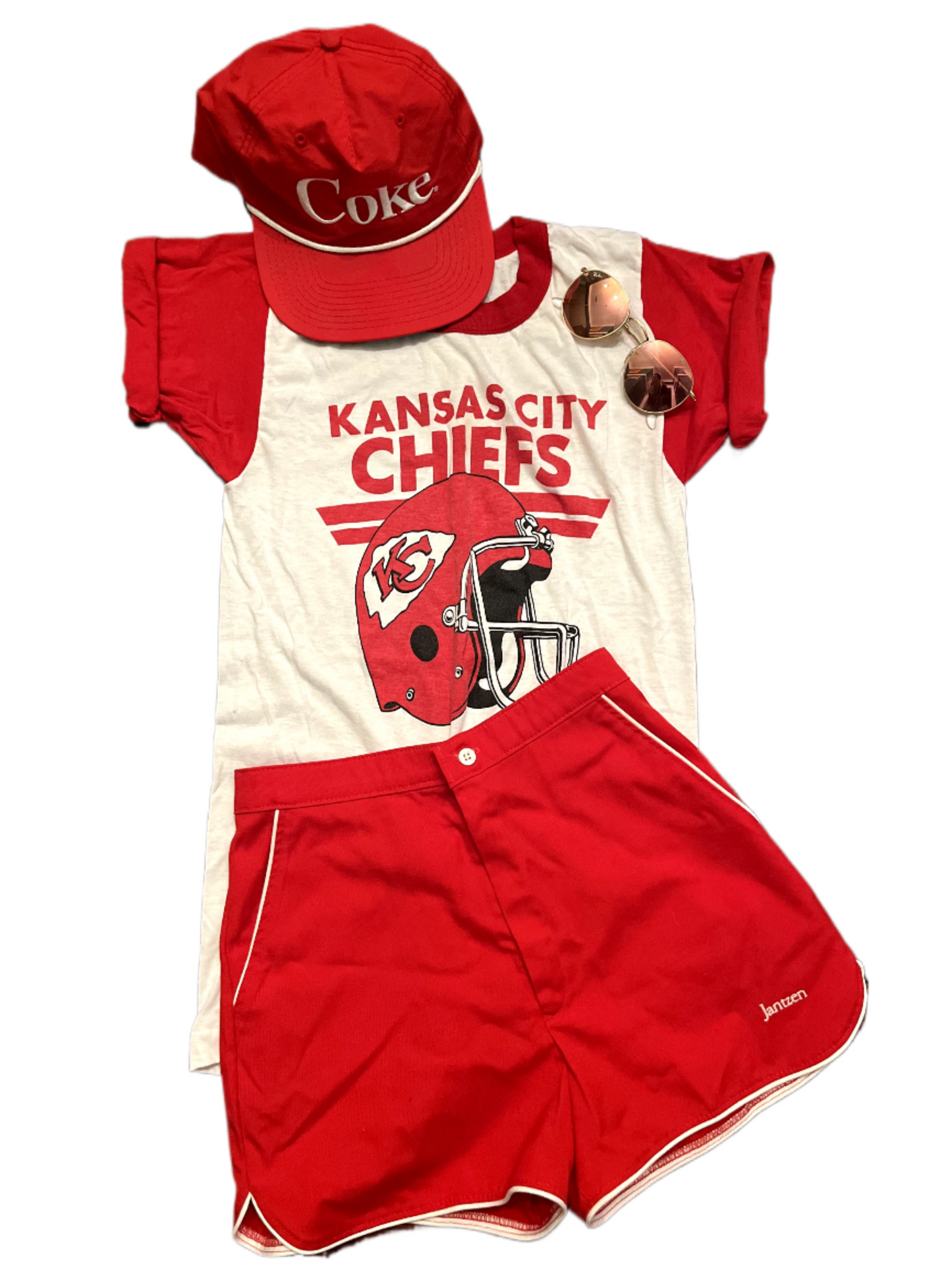 Lay down image of KC Chiefs tee styled with red shorts, red hat and sunglasses.