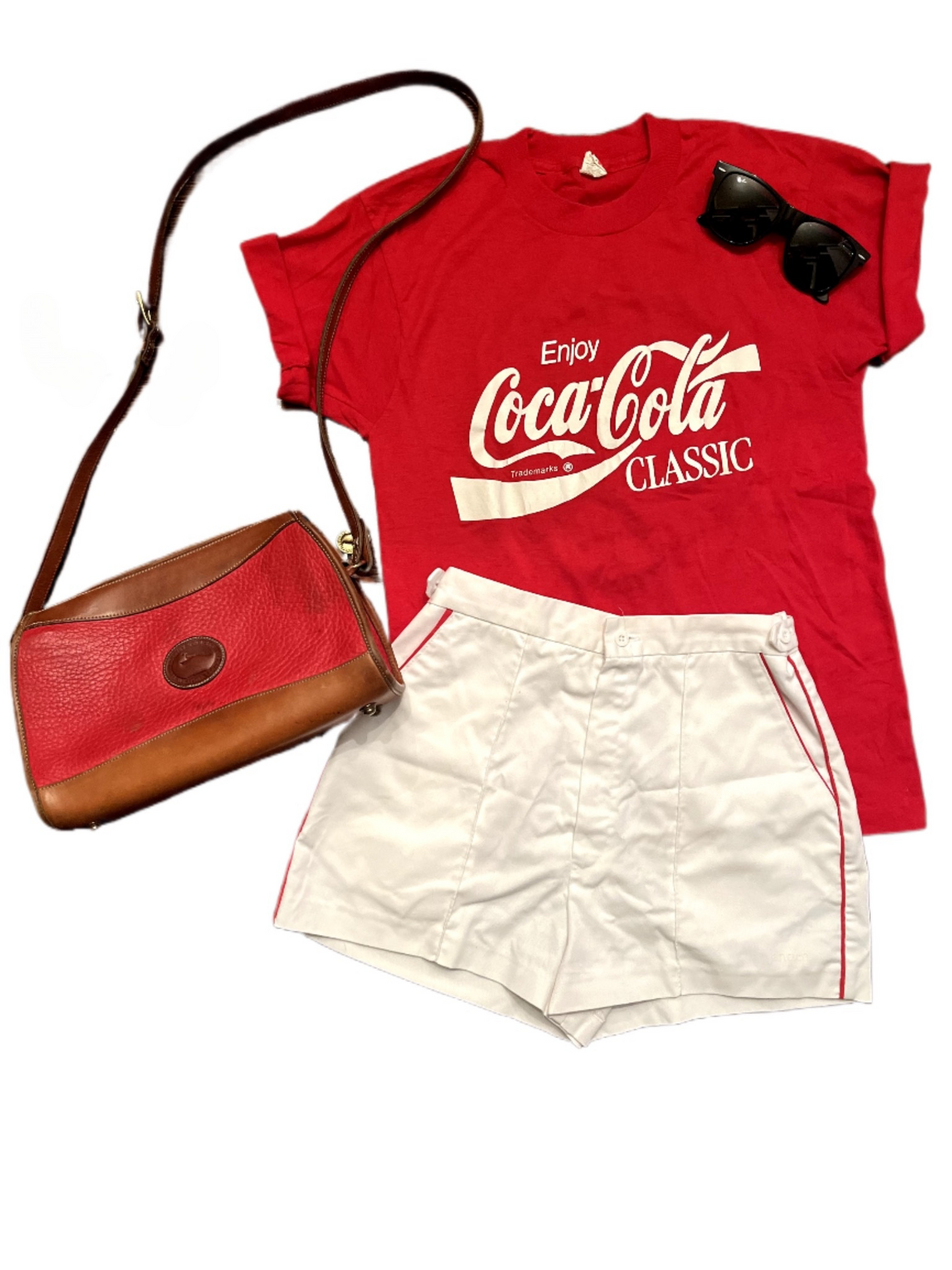 Lay down image of red Dooney and Bourke purse with red coca-cola tee, white shorts and sunglasses
