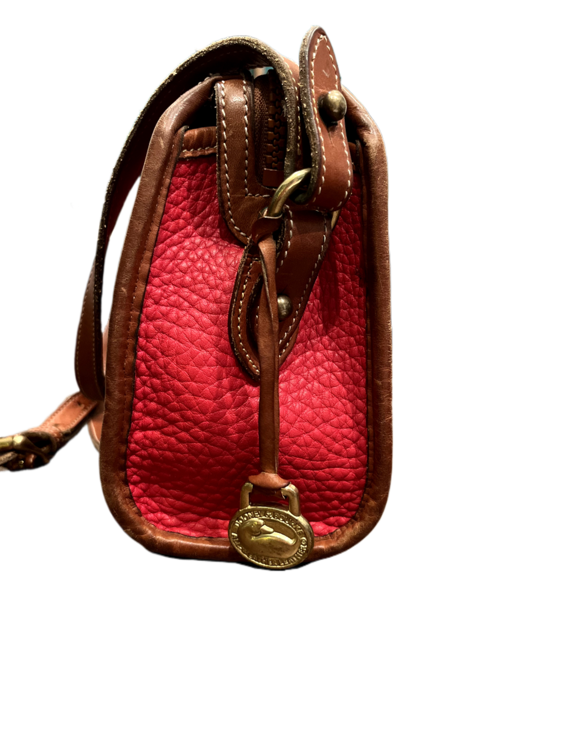 Side view of red Dooney & Bourke purse with tan leather strap and brass charm on white background.