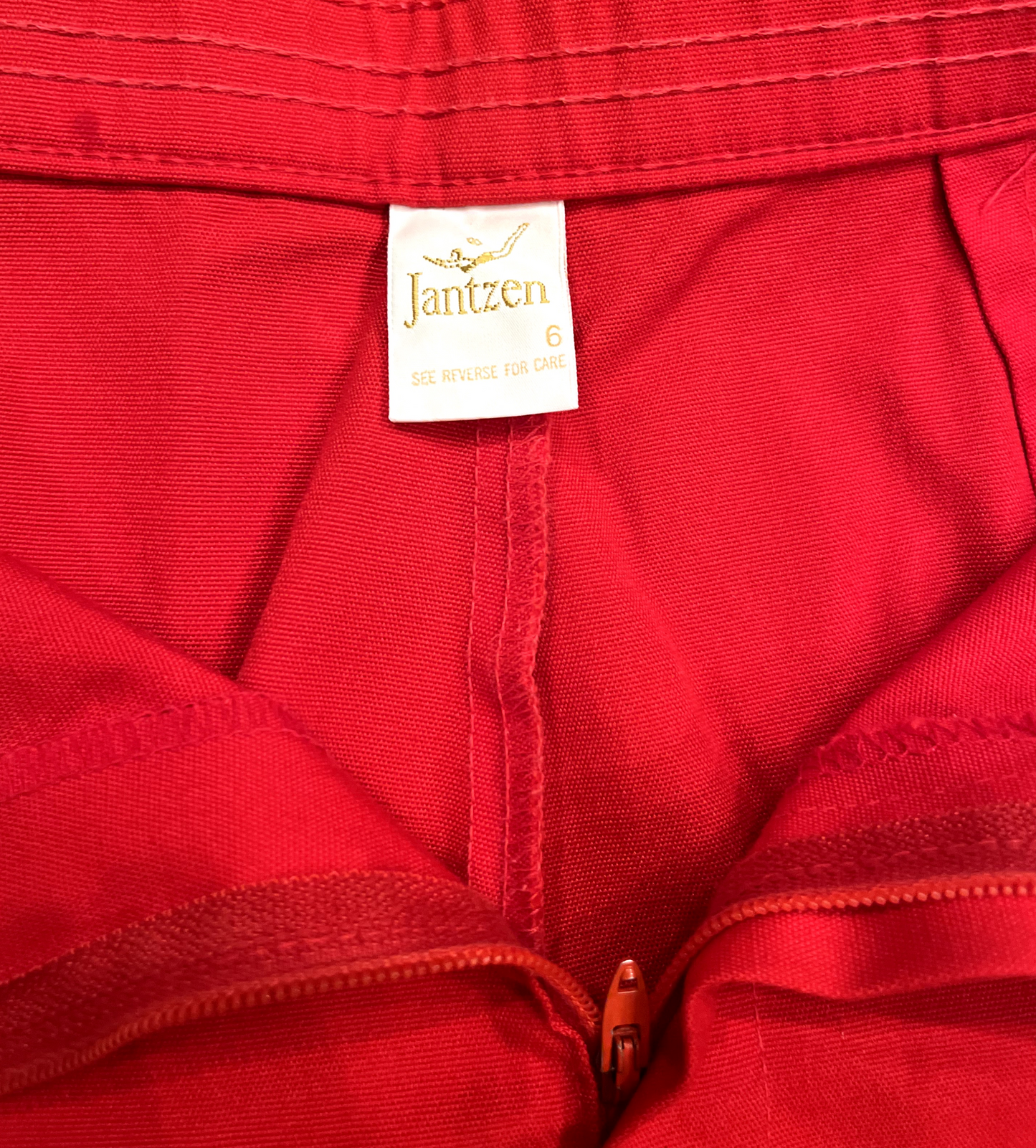 Close up of Jantzen label vintage red shorts with white stripe on white background.