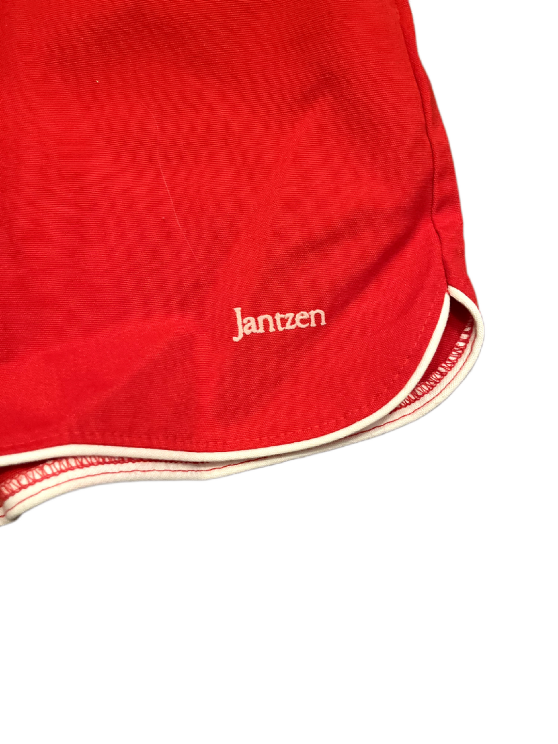 Jantzen logo on front of vintage red shorts with white stripe on white background.