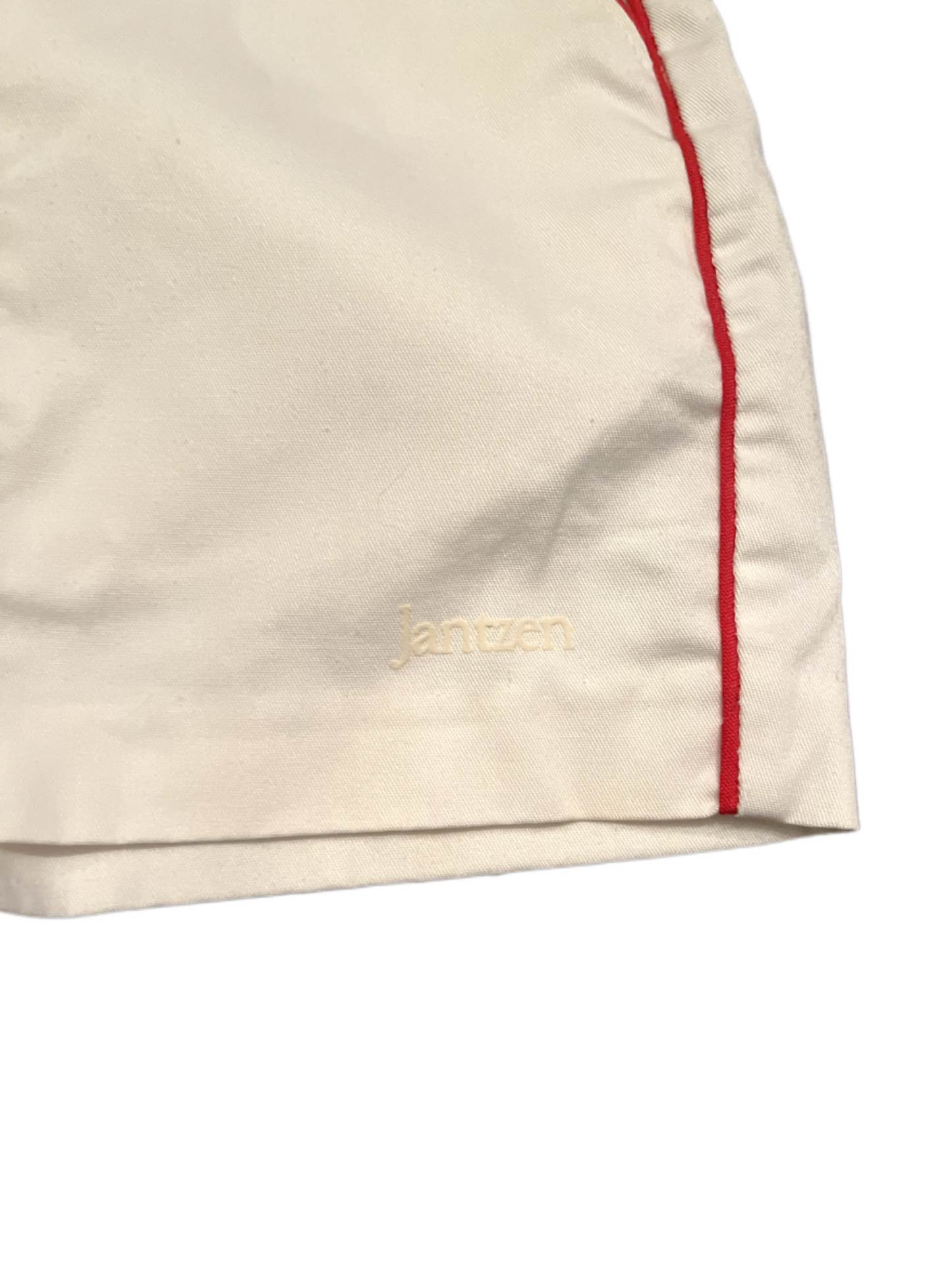Jantzen logo on front of white shorts with red stripe on white background.