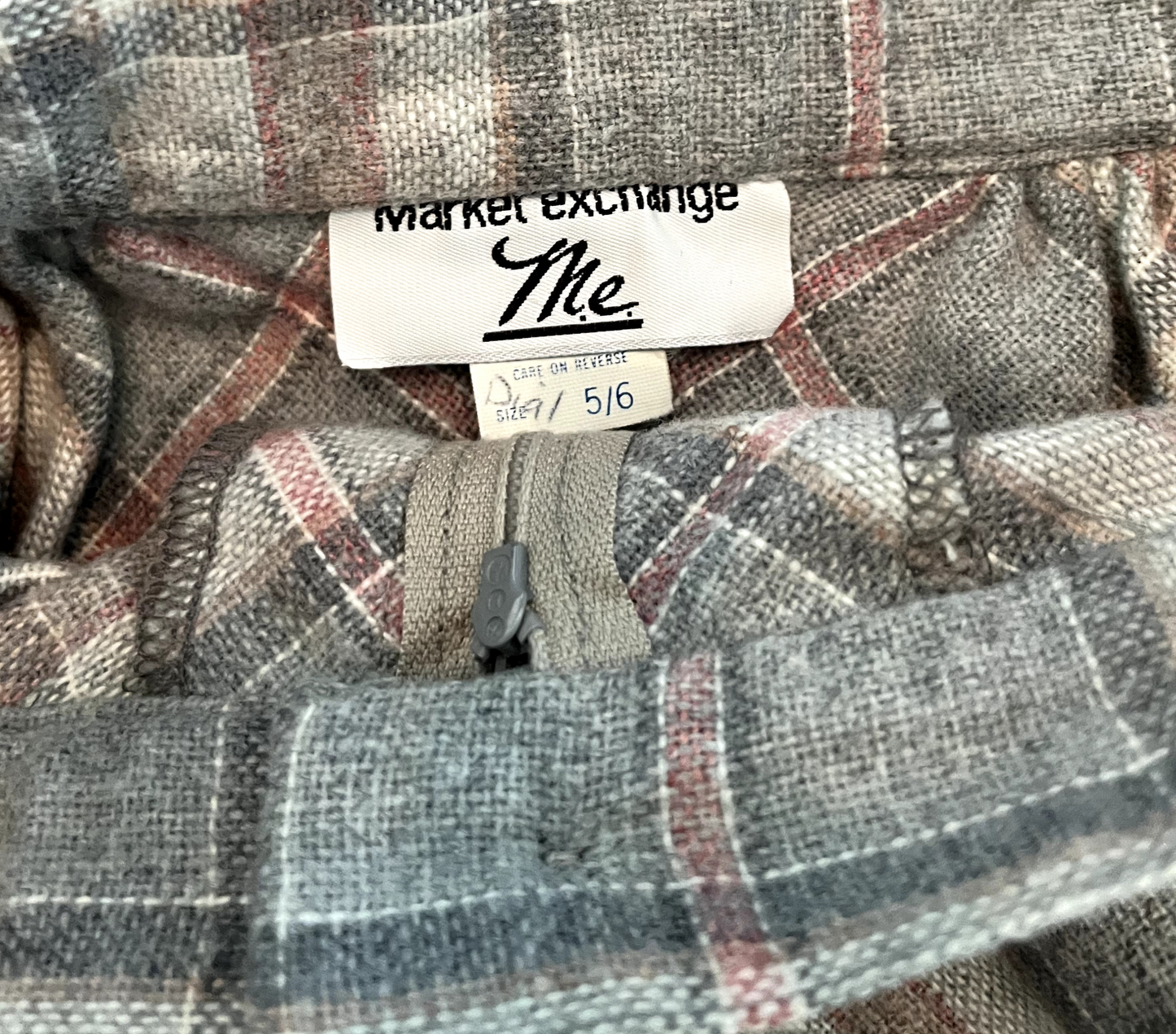 Vintage ladies 7/8ths plaid skirt in pink, grey and white with front zipper and button on white background closeup image of sewn in label.